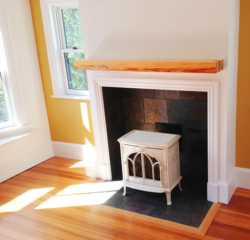 Jotul gas stove with slate hearth and surround.  Baseboard trim, window casings, and a floating mantel made from a reclaimed beam of Southern yellow pine.